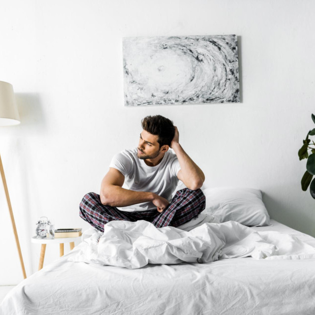 handsome pensive man in pajamas sitting on bed in the morning