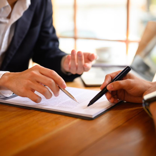 Closeup lawyer or insurance agent pointing at contract showing male client where to signature sign.