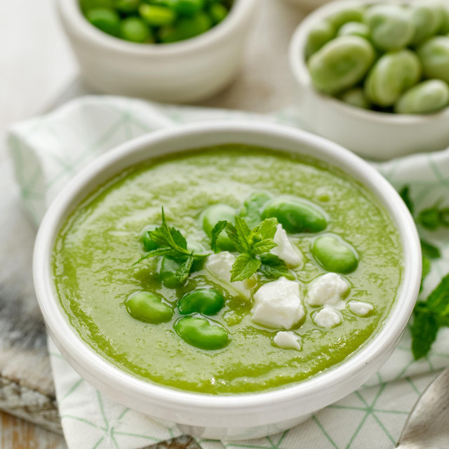 Broad bean soup with fresh mint and feta cheese in a white bowl on a wooden table. Healthy and delicious vegetarian food