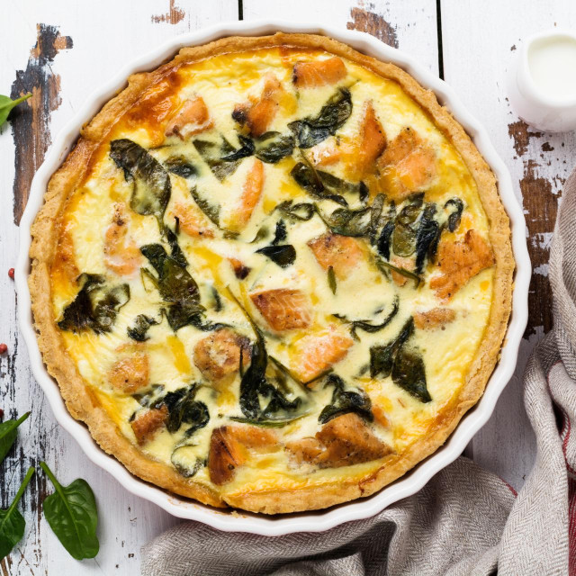 Homemade quiche tart with red fish and spinach on light wooden background. Vintage style. Top view.