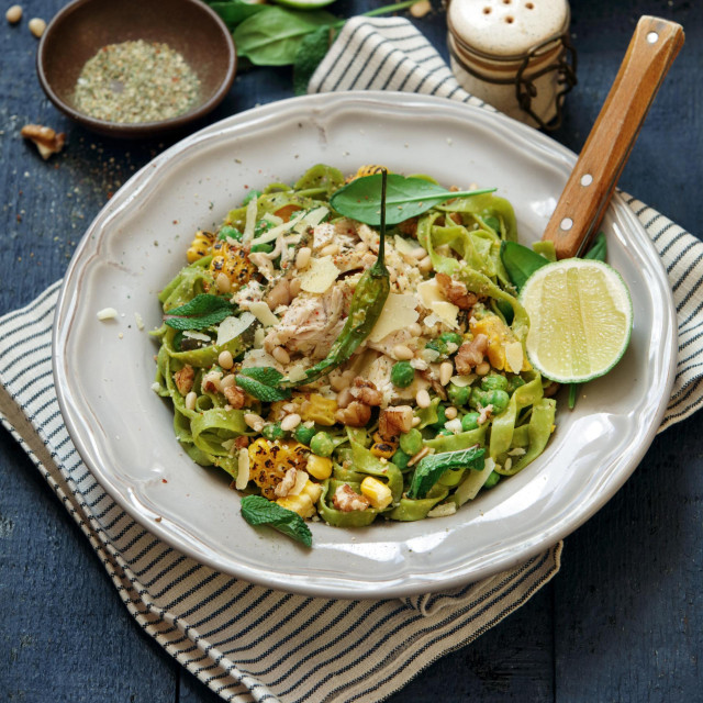 Leftover chicken breast green pasta with basil-mint pesto, sweet corn, green peas, seeds and microgreen. Close-up composition on dark wooden background.