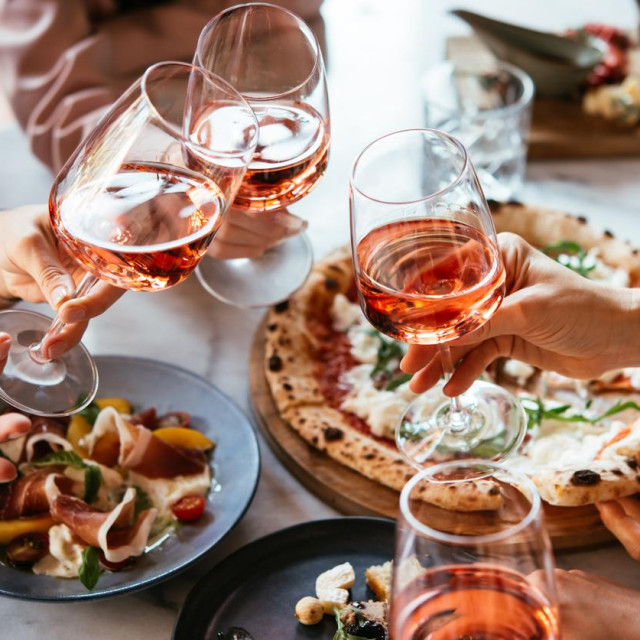 Friends enjoy a dinner party with pizza and rose wine in a bar or a restaurant.