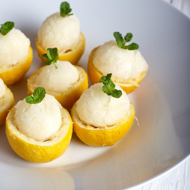 Lemon icecream served in half of lemon in white plate on white background. Ice creame scoop near it.