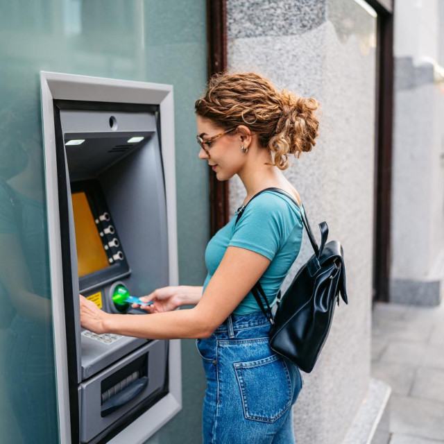 Young woman withdrawing money using a credit card at the ATM machine on the street in Budapest in Hungary.