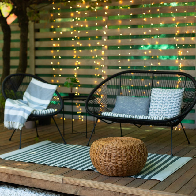 Terrace house with plants, wooden wall and table, comfortable sofa, armchair and lanterns. Cozy space in patio or balcony. Wooden veranda with garden furniture. Modern lounge outdoors in backyard