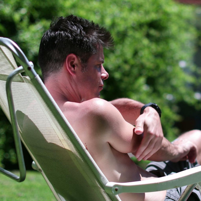 Man scratching arm removing mosquito away, resting outside in backyard garden