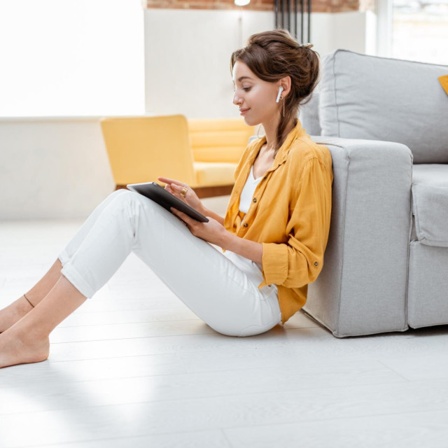 Young and cheerful woman working on digital tablet while sitting relaxed on the floor at home. Concept of leisure, freelance and mobile work