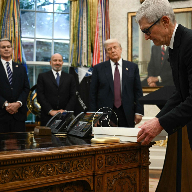 Izvršni direktor Applea Tim Cook izlaže suvenir na Resolute Desku u Ovalnom uredu Bijele kuće u Washingtonu, DC, 6. kolovoza 2025. dok američki predsjednik Donald Trump (2. desno), ministar trgovine Howard Lutnick (2. lijevo) i ministar financija Scott Bessent (lijevo) promatraju prije nego što objave da će Apple uložiti dodatnih 100 milijardi dolara u Sjedinjene Države, čime će ukupna obećana ulaganja u sljedeće četiri godine dosegnuti 600 milijardi dolara.