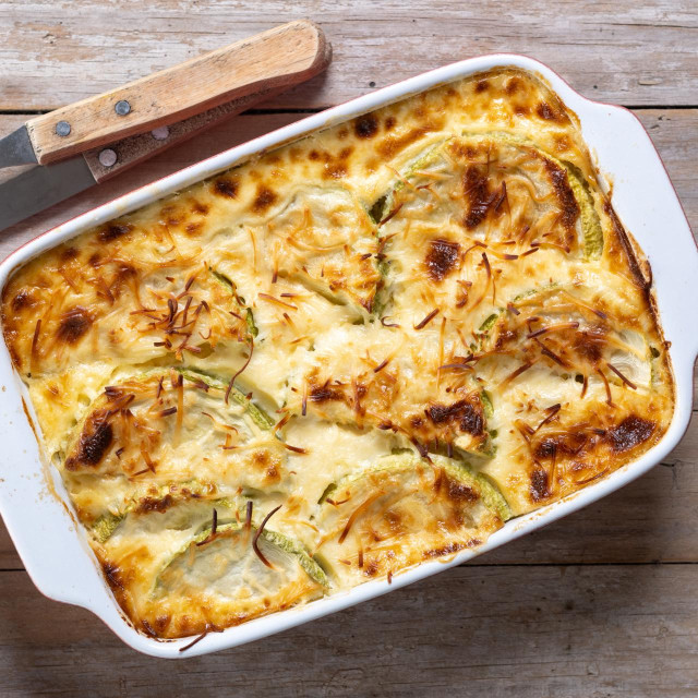 Casserole with cheese and gratin zucchini on wooden table