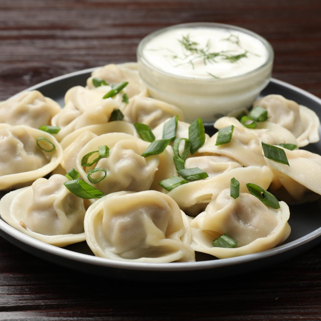 Delicious pelmeni with green onion served on wooden table, closeup