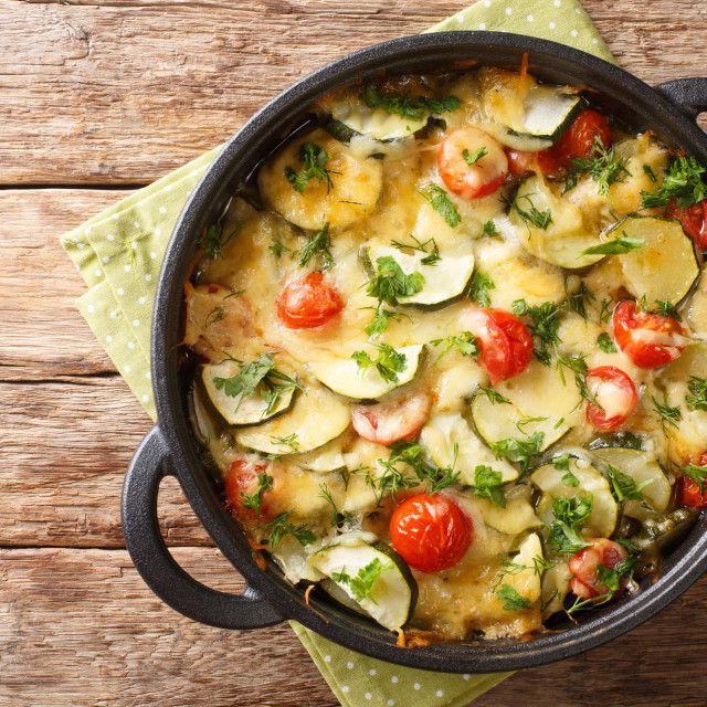 Zucchini summer casserole with cheese and cherry tomatoes close-up in a pan on the table. horizontal top view from above
