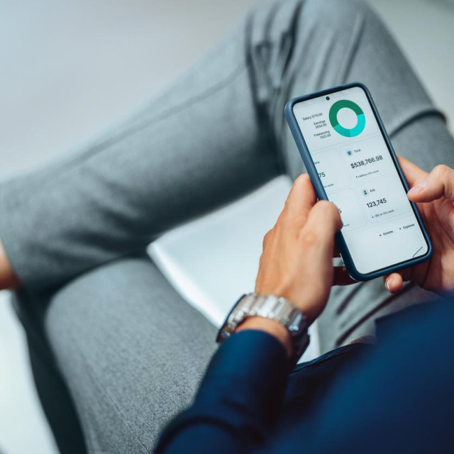 Close-up of a man checking financial data on a smartphone. Display shows detailed statistics and graphs, suggesting productivity and business analysis.