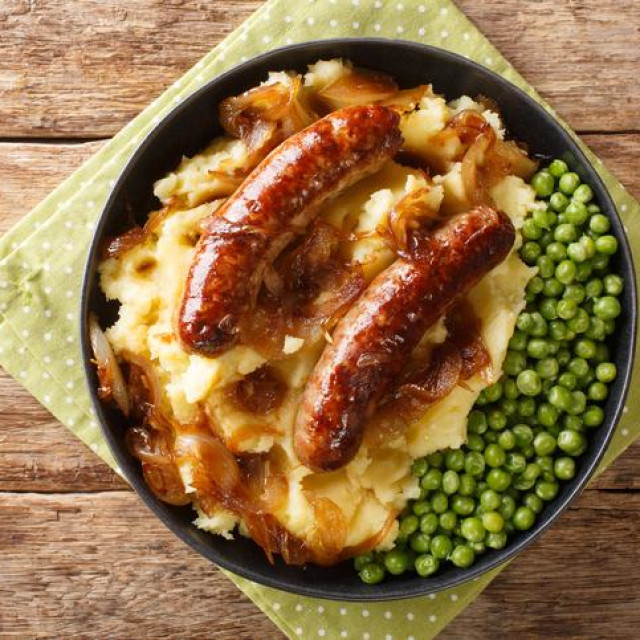 Fried sausages with mashed potatoes, onion gravy and green peas close-up in a plate on the table. horizontal top view from above