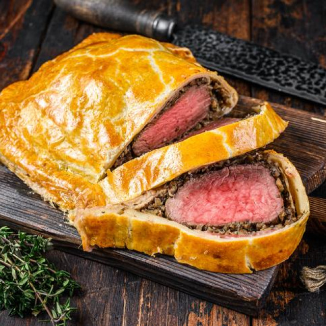 Homemade Beef Wellington puff pie with tenderloin meat on a cutting board. Dark wooden background. Top view.