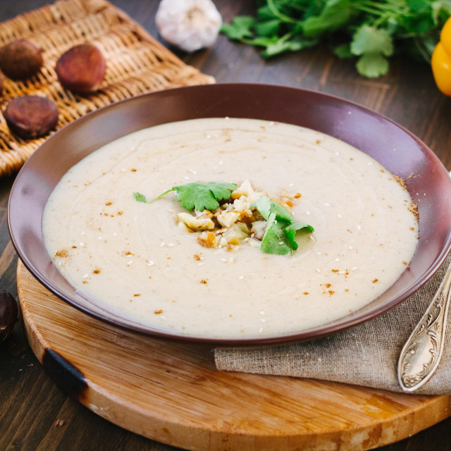 Chestnut cream soup on brown plate with vegetables.