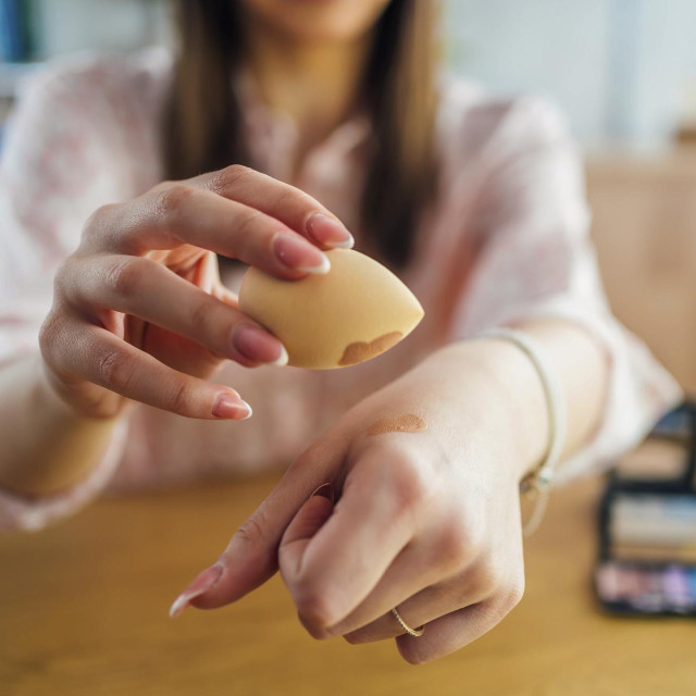 Woman holding beauty blender sponge with foundation on him. Makeup, beauty concept.