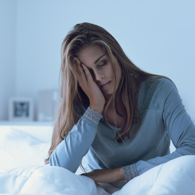 Depressed woman awake in the night, she is touching her forehead and suffering from insomnia