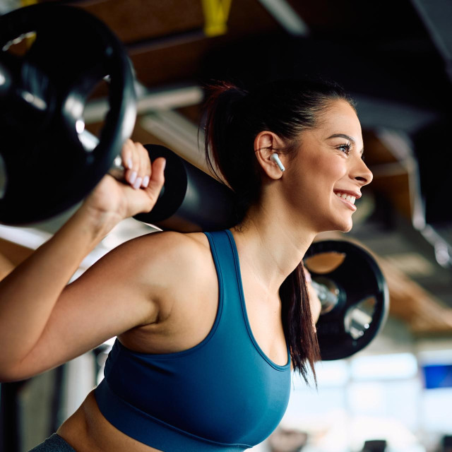Happy athletic woman working out with a barbell during weightlifting training in a gym.