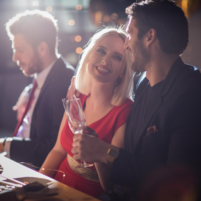 Christmas dinner with friends. Home is decorated with Christmas string lights. Everyone wearing elegant clothing. Eating sushi and drinking champagne.