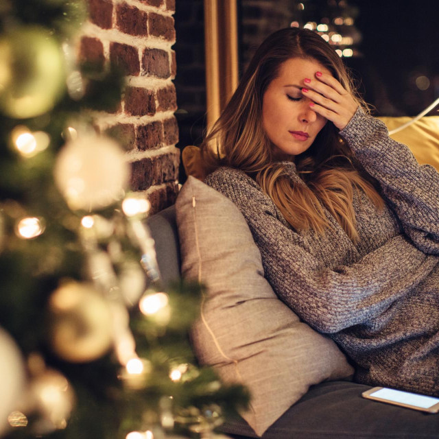 Depressed mid adult woman near christmas tree in her home.
