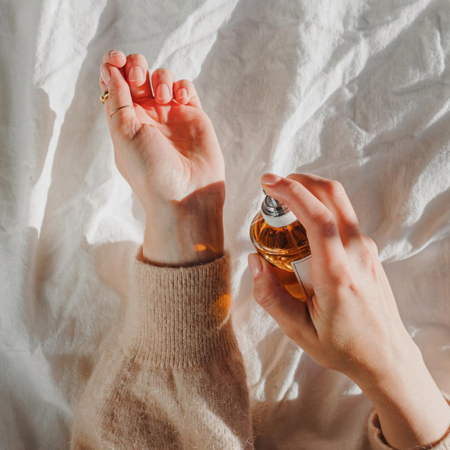 Female hands holding a bottle of perfume in natural morning light, overhead view