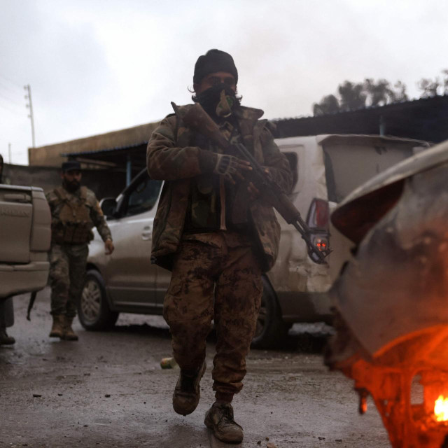 Pripadnici snaga sirijskog Ministarstva obrane promatraju zapaljeno vozilo u Raki, gradu na sjevernoj obali rijeke Eufrat, 18. siječnja 2026