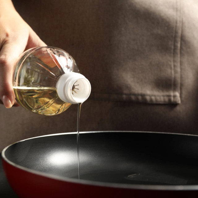 Woman pouring oil into frying pan at table, closeup