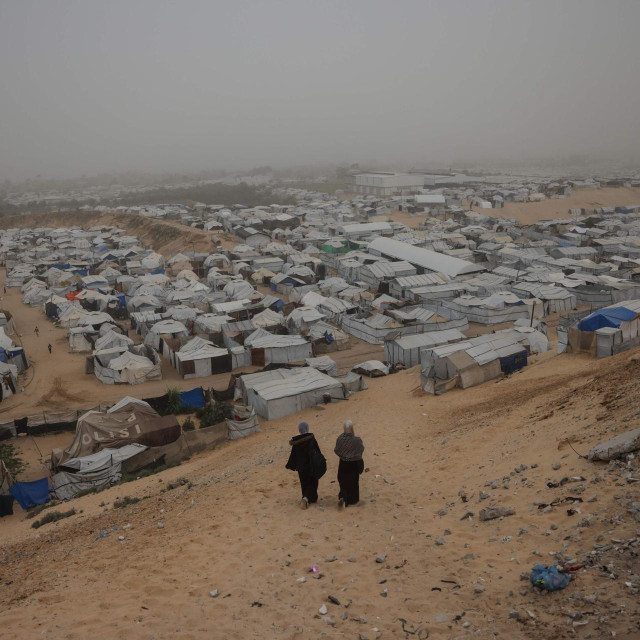 Žene se 14. veljače 2026. spuštaju niz padinu s koje se pruža pogled na kamp za raseljene Palestince u Han Junisu, na jugu Pojasa Gaze