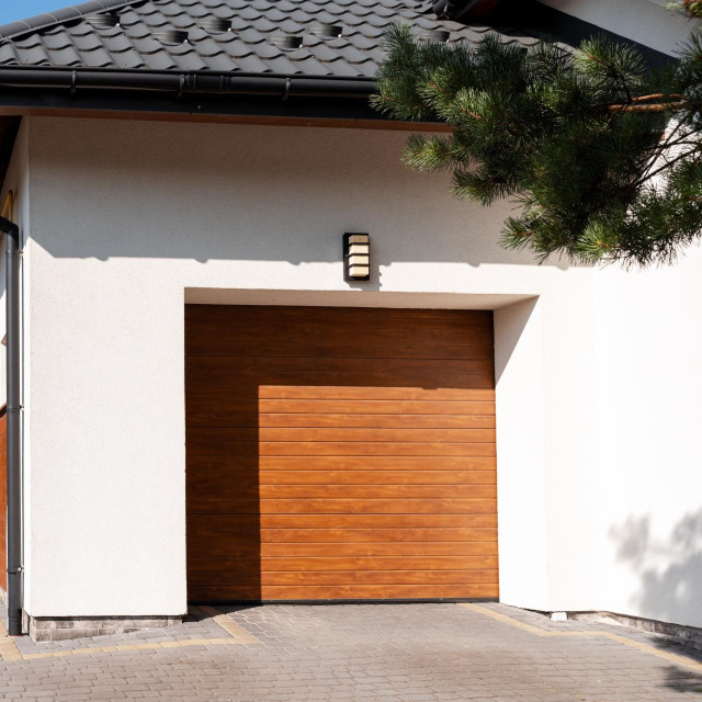 Wooden garage door complementing a modern white house, featuring a paved driveway and lush greenery enhancing the inviting exterior