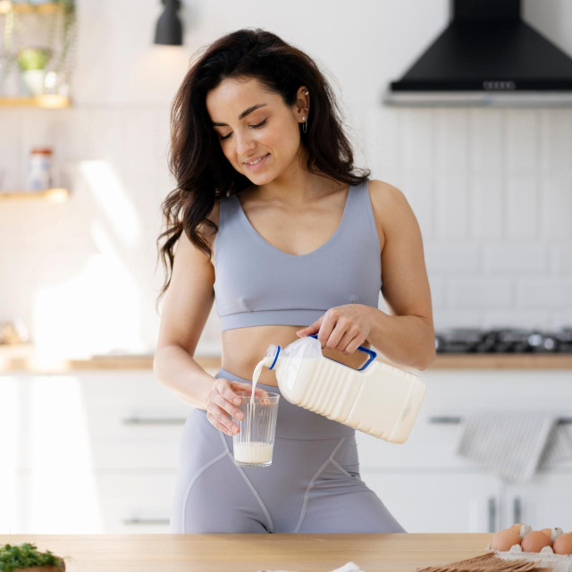 Portrait of beautiful smiling fit woman drinking fresh milk, cooking breakfast standing in modern kitchen. Healthy lifestyle concept