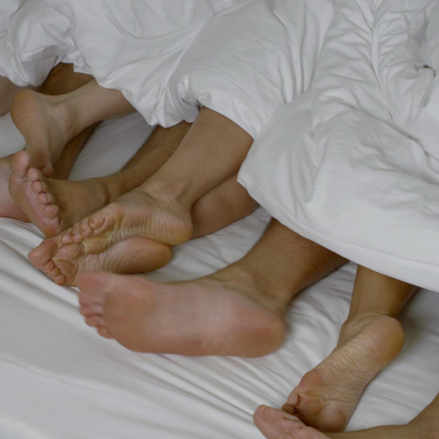 barefoot bound men and women legs sticking out moving from under the white bedspread on the bed close up slow motion