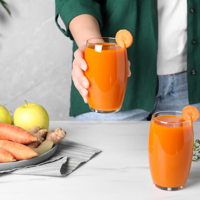 Woman holding glass with carrot juice, closeup
