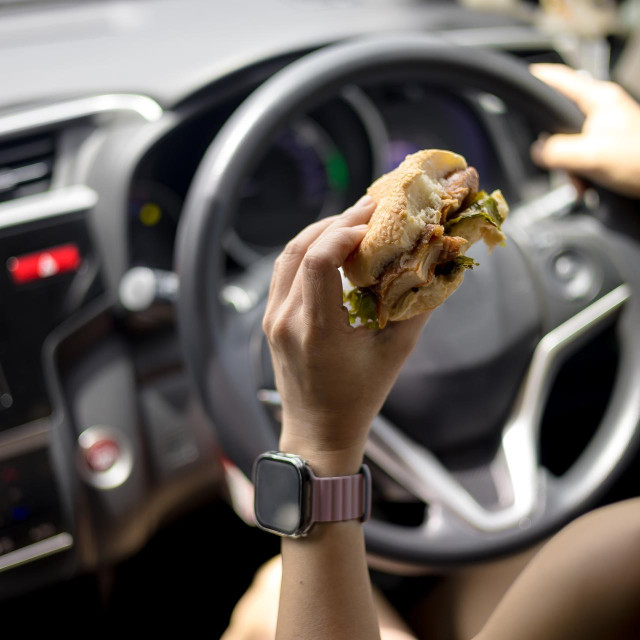 Woman is eating a hamburger while driving to work in the morning