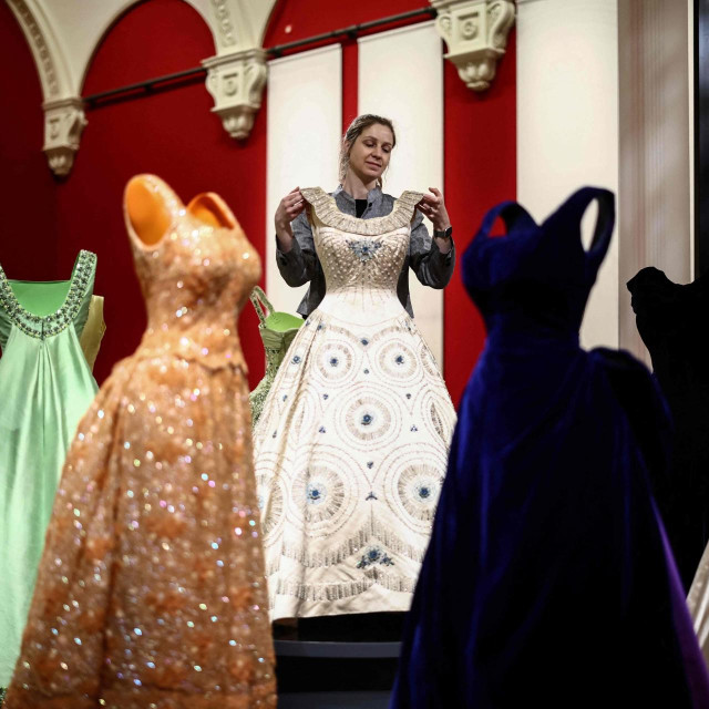 A member of the Royal Collection Trust staff (C) poses amongst the evening gown collection, during a media preview of the exhibition ‘Queen Elizabeth II: Her Life in Style‘ at the King�s Gallery in Buckingham Palace in London on April 9, 2026. The largest exhibition showcasing Queen Elizabeth II�s fashion ever staged is being held from April 10 to October 18, 2026. (Photo by Henry NICHOLLS/AFP)/RESTRICTED TO EDITORIAL USE - NO MARKETING - NO ADVERTISING CAMPAIGNS