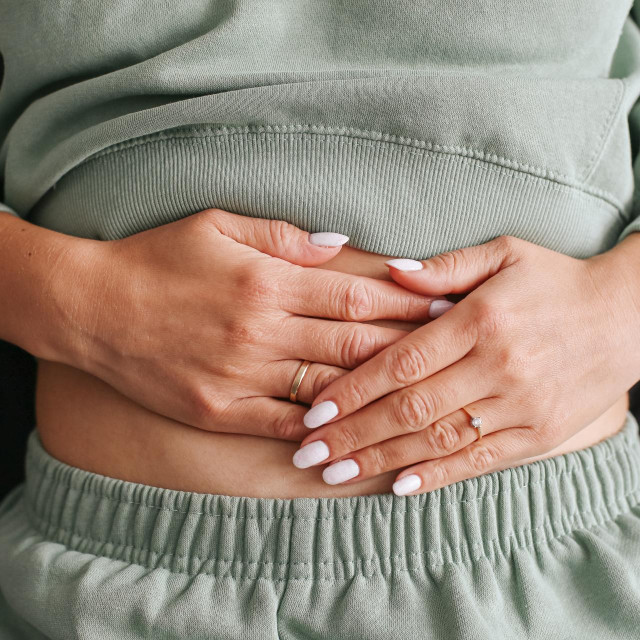 Woman holding stomach with hands. Menstrual pain and stomachache concept. Female body language showing discomfort. Natural lifestyle health issue. Everyday problem and physical symptom.