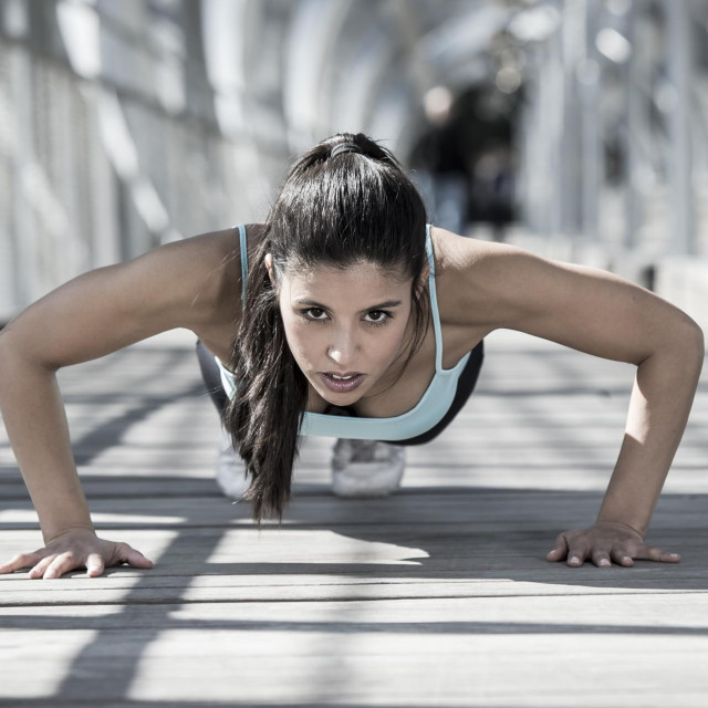 young beautiful and athletic sport woman doing push up before running in urban training workout on modern metal city bridge in female runner body care concept