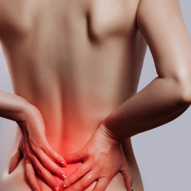 Woman having backache, pain back isolated on gray background. Scoliosis. Spinal cord problems on womans back. Beautiful naked woman touching her back.