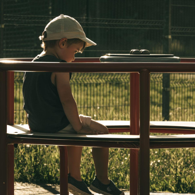 Lonely child sits on a playground carousel, a sad boy without friends has no company to play with