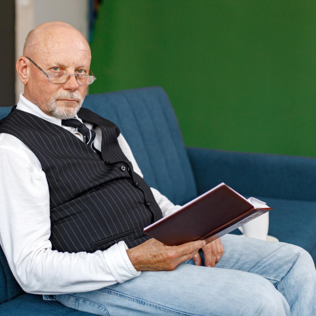 Mature man reading a book and drinking a tea on the sofa in living room