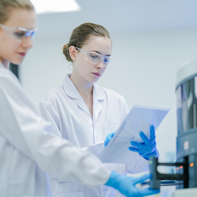 researchers in white lab coats discussing experimental results near an automated analyzer. Dedicated specialists managing pharmaceutical trials and biotech innovation in a sterile environment.