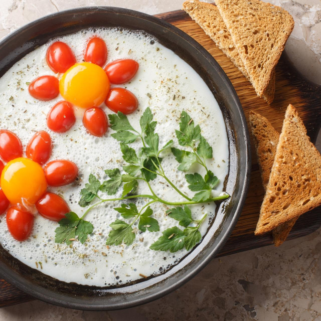 Flower shaped breakfast idea cooked fried eggs, parsley and cherry tomatoes close-up in a plate on the table. Horizontal top view from above