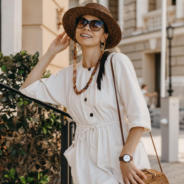 attractive woman walking in street on vacation dressed in white summer fashion dress straw hat sunglasses and purse, smiling happy having fun, stylish accessories trend