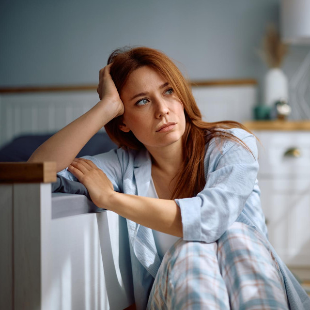 Pensive woman thinking of her problems while sitting in her bedroom.