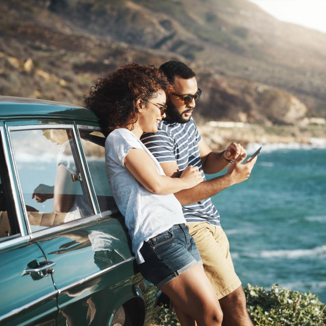 Shot of a young couple using a mobile phone on a road trip