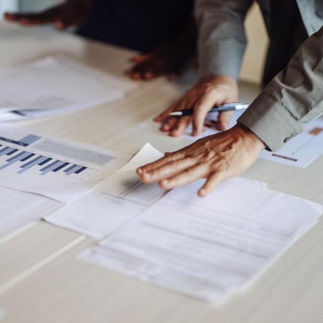 Professional teamwork showcasing colleagues reviewing financial data, graphs, and documents on a desk; Represents discussion, collaboration, and productivity in achieving business goals