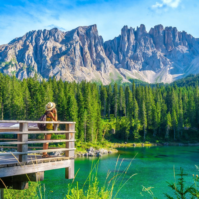 Female tourist admiring the stunning landscape of lake carezza with the latemar massif in the background, a popular destination in the italian dolomites