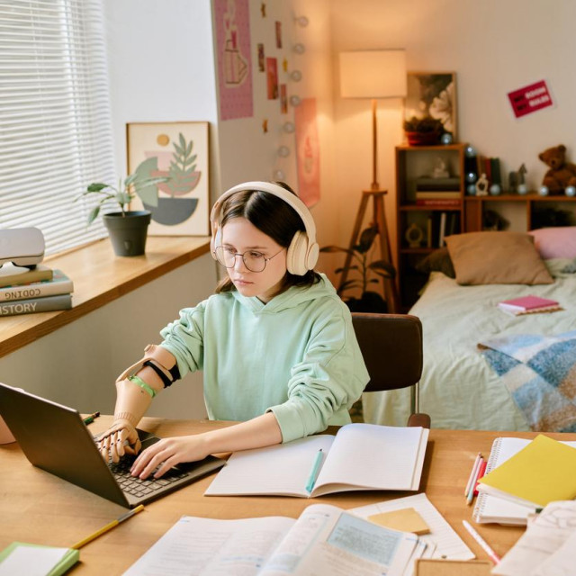 Teenager with prosthetic hand focusing on work in well-decorated bedroom with various posters and decorations around