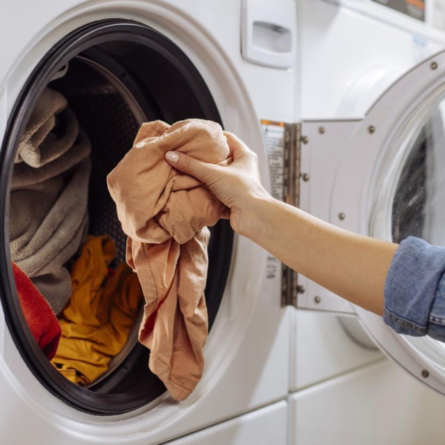 Close up of an unrecognizable woman putting dirty clothes and laundry into washing machine