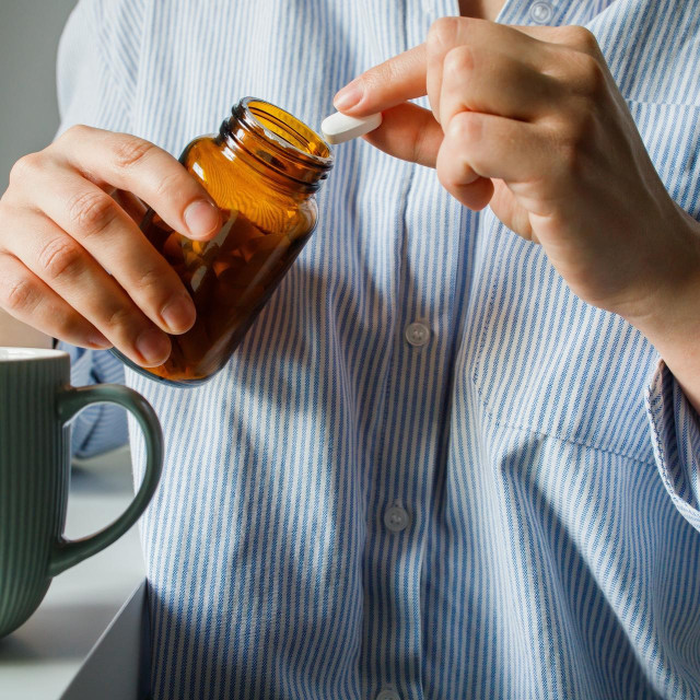 Woman taking pills from small brown glass bottle and drinking water close up. Home treatment, drinking antidepressants, woman‘s health, healthcare and medicine, biohacking