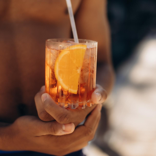 Close-up of a muscular man enjoying a refreshing aperol spritz cocktail on a sunny beach, capturing the essence of summer leisure and relaxation